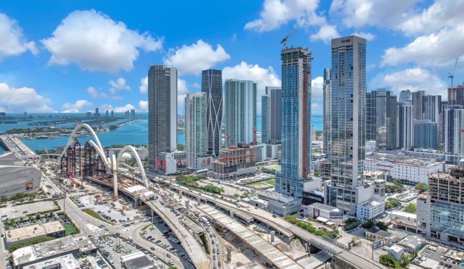 Aerial view of the Downtown Miami and Edgewater skyline over Biscayne Bay, with high-rise condominium towers along I-395 and the Signature Bridge under construction